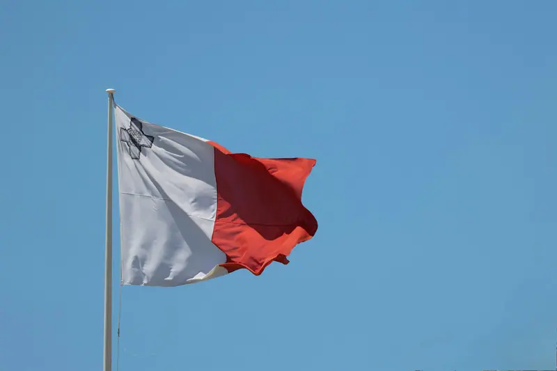 The flag of malta waves against a clear blue sky.