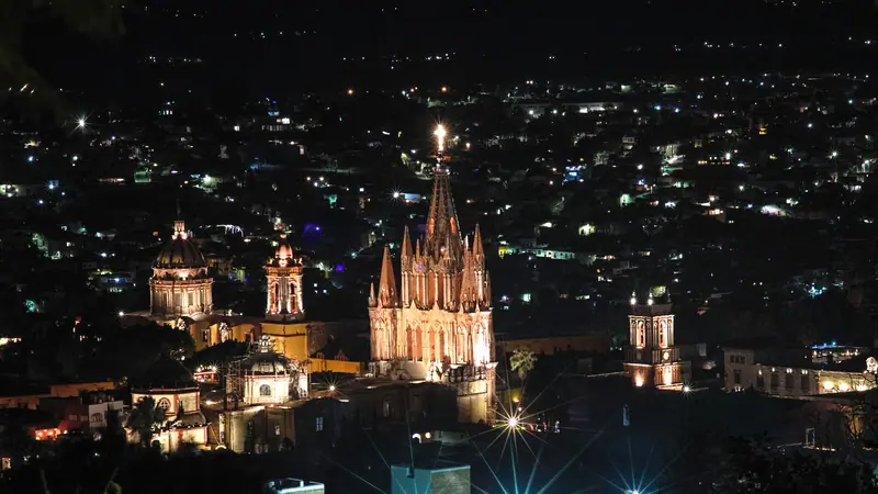 Die beleuchtete Parroquia von San Miguel de Allende in Mexiko bei Nacht über der Stadt