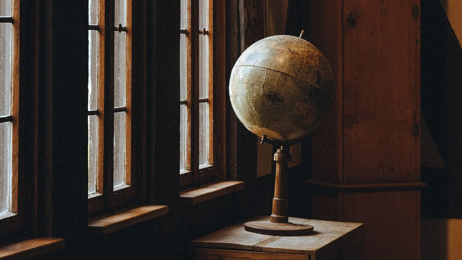 Antique globe on a wooden table beside tall windows
