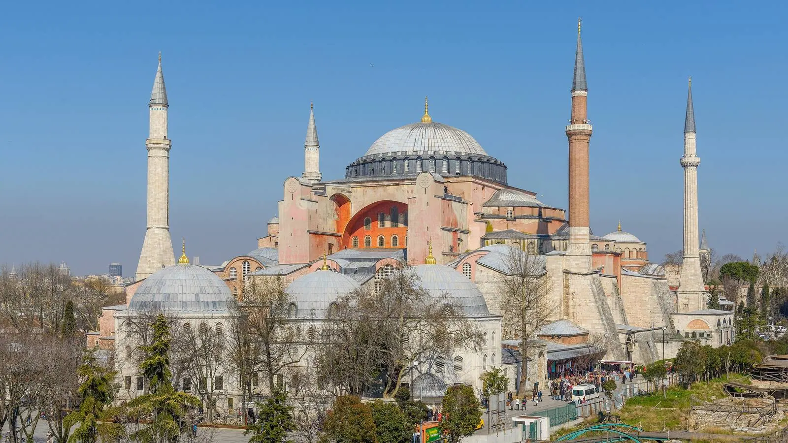 Hagia Sophia in Istanbul with its great dome, buttresses and four minarets under a clear blue sky, bare trees in the foreground.