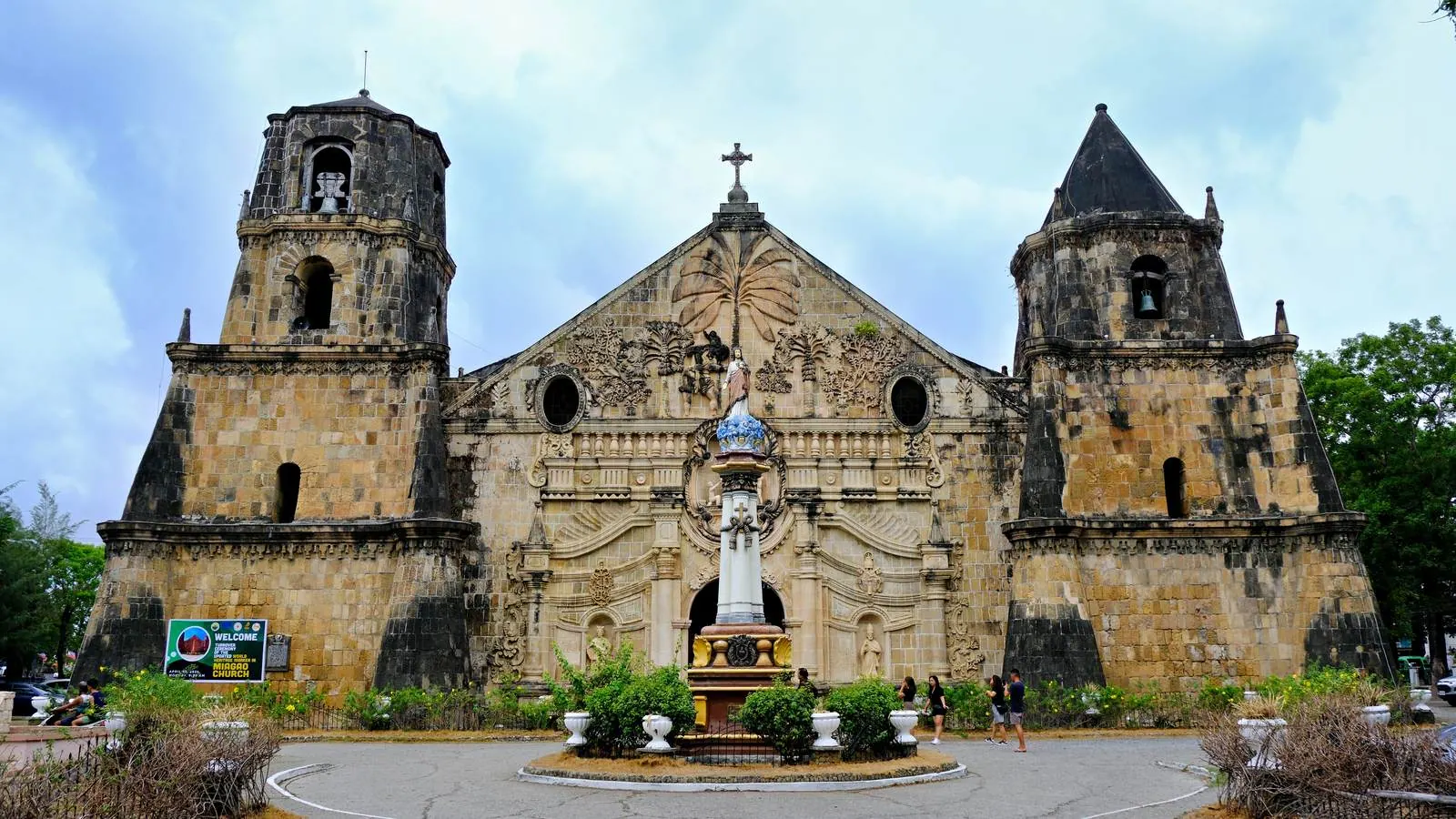 The baroque stone facade and two fortress-like bell towers of Miagao Church in Iloilo, the Philippines, under a cloudy sky.