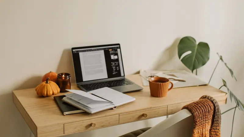 Heller Schreibtisch zu Hause im Herbst mit Laptop, aufgeschlagenem Planer, Tasse und Zeitung, der Ort für die Steuererklärung vor dem 31. Oktober.